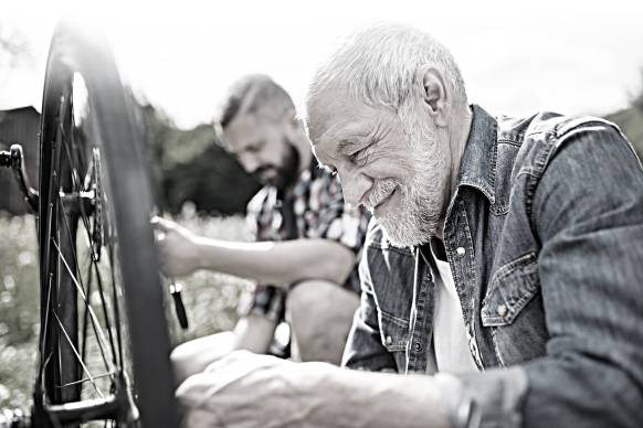 Dos hombres, uno anciano y otro de mediana edad, reparan una bicicleta.