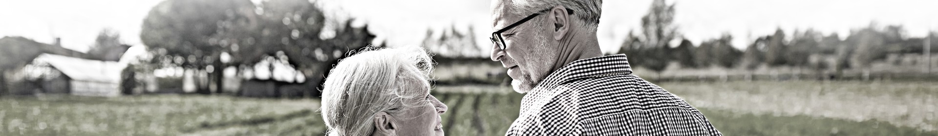 An elderly couple gaze into each others' eyes while standing in front of a field.
