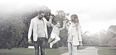 A father and mother play with their daughter by holding her hands.