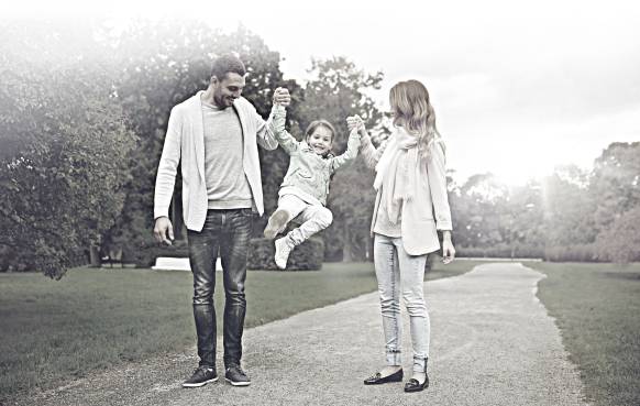 Un padre y una madre juegan con su hija tomándola de la mano.