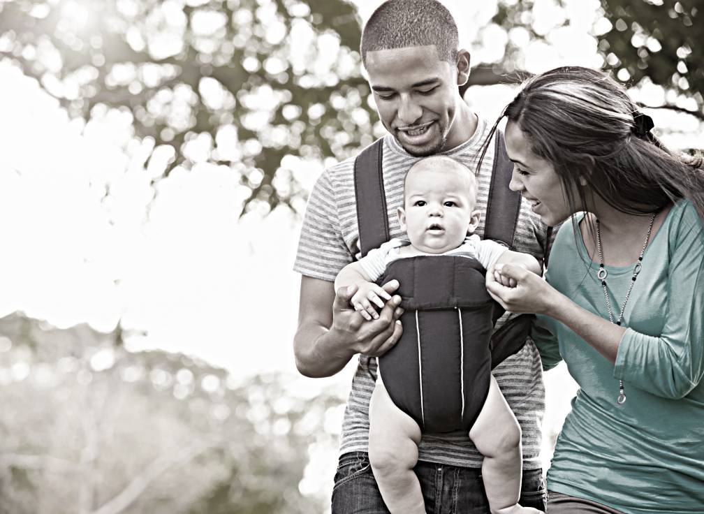 A father and mother looking at their infant child while outside walking.